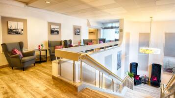 Eine Hotelhalle mit Holzboden, einer Sitzecke mit Sofas, einer Treppe und Kunstwerken an den Wänden.