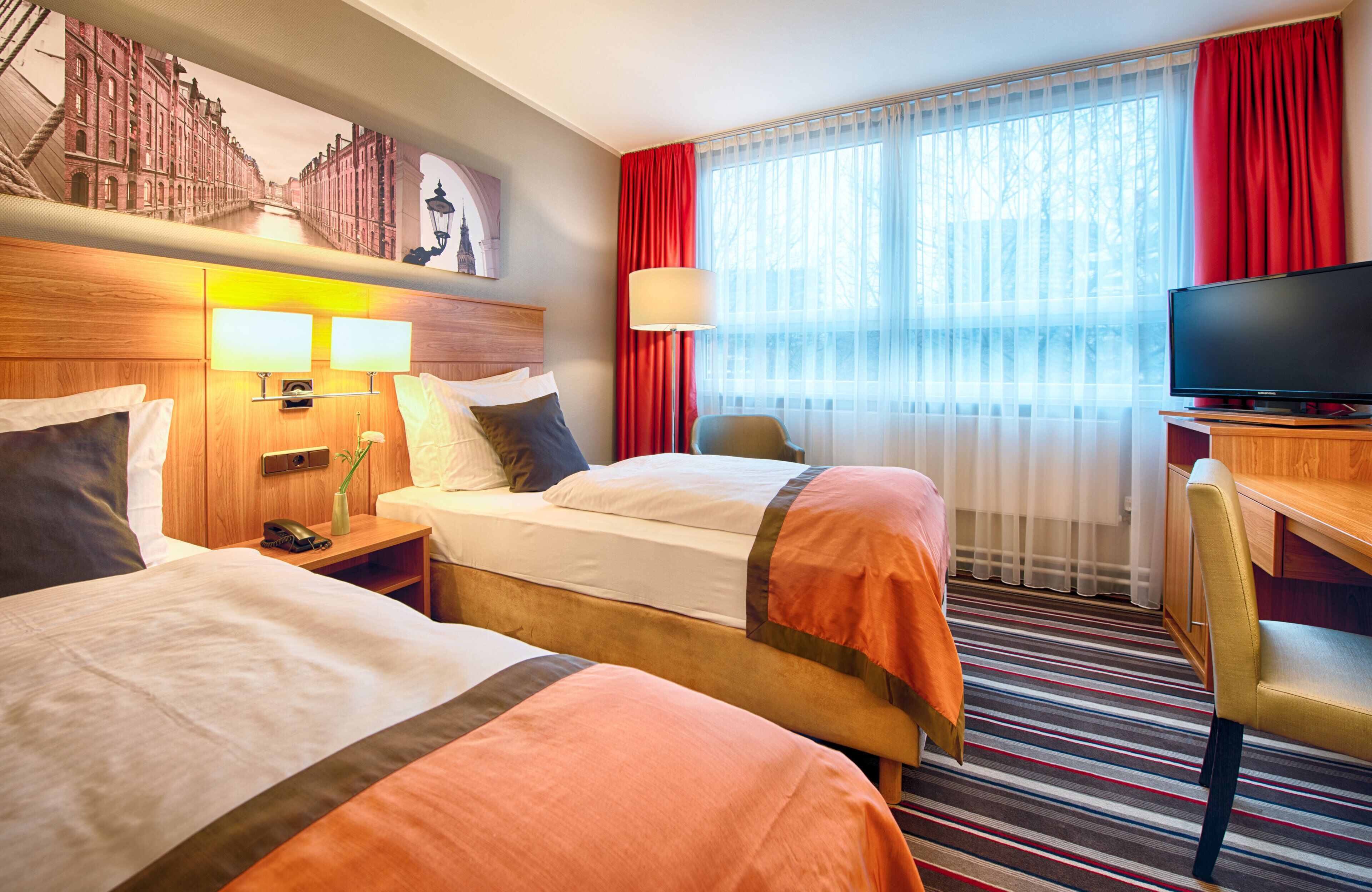 A hotel room with two beds, a television, a desk, and a window with curtains.