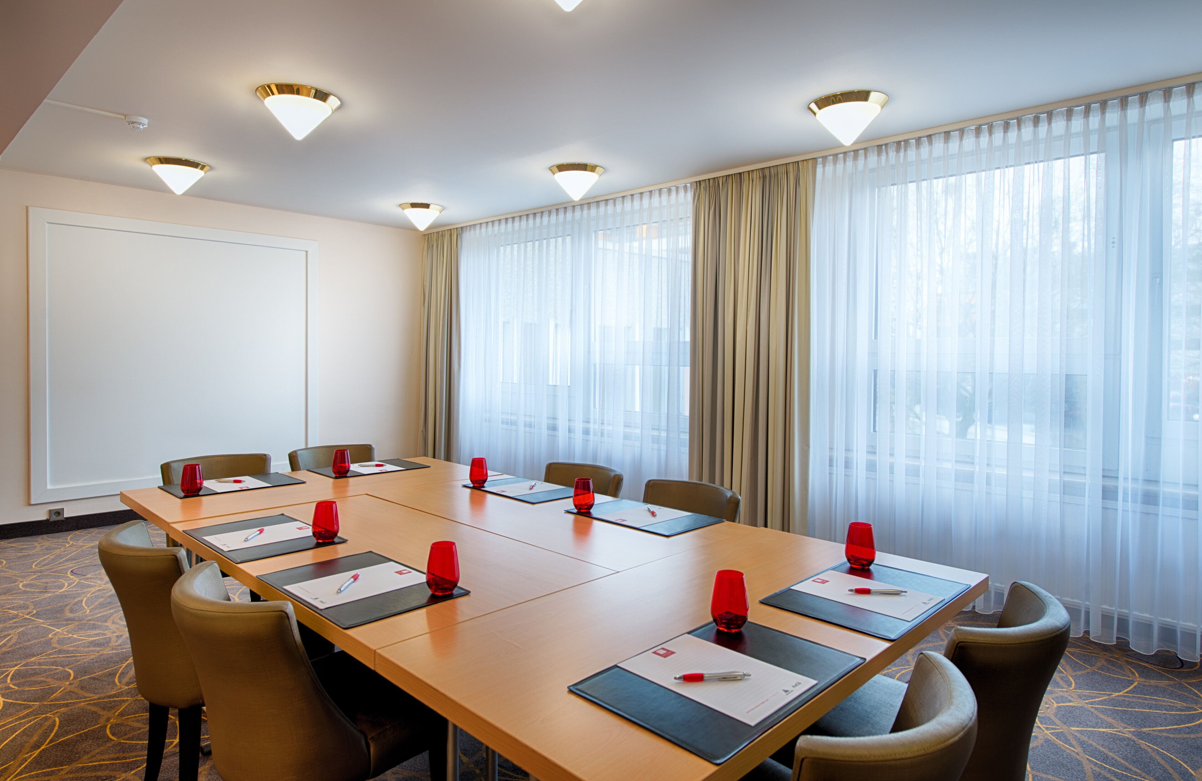 Uma sala de conferências com uma mesa comprida, cadeiras e uma tela de projetor.