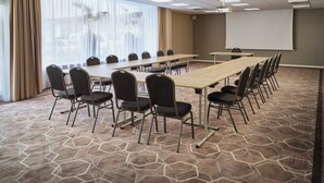 Una sala de conferencias con una larga mesa, sillas, una pantalla de proyector y un amplio ventanal con cortinas.