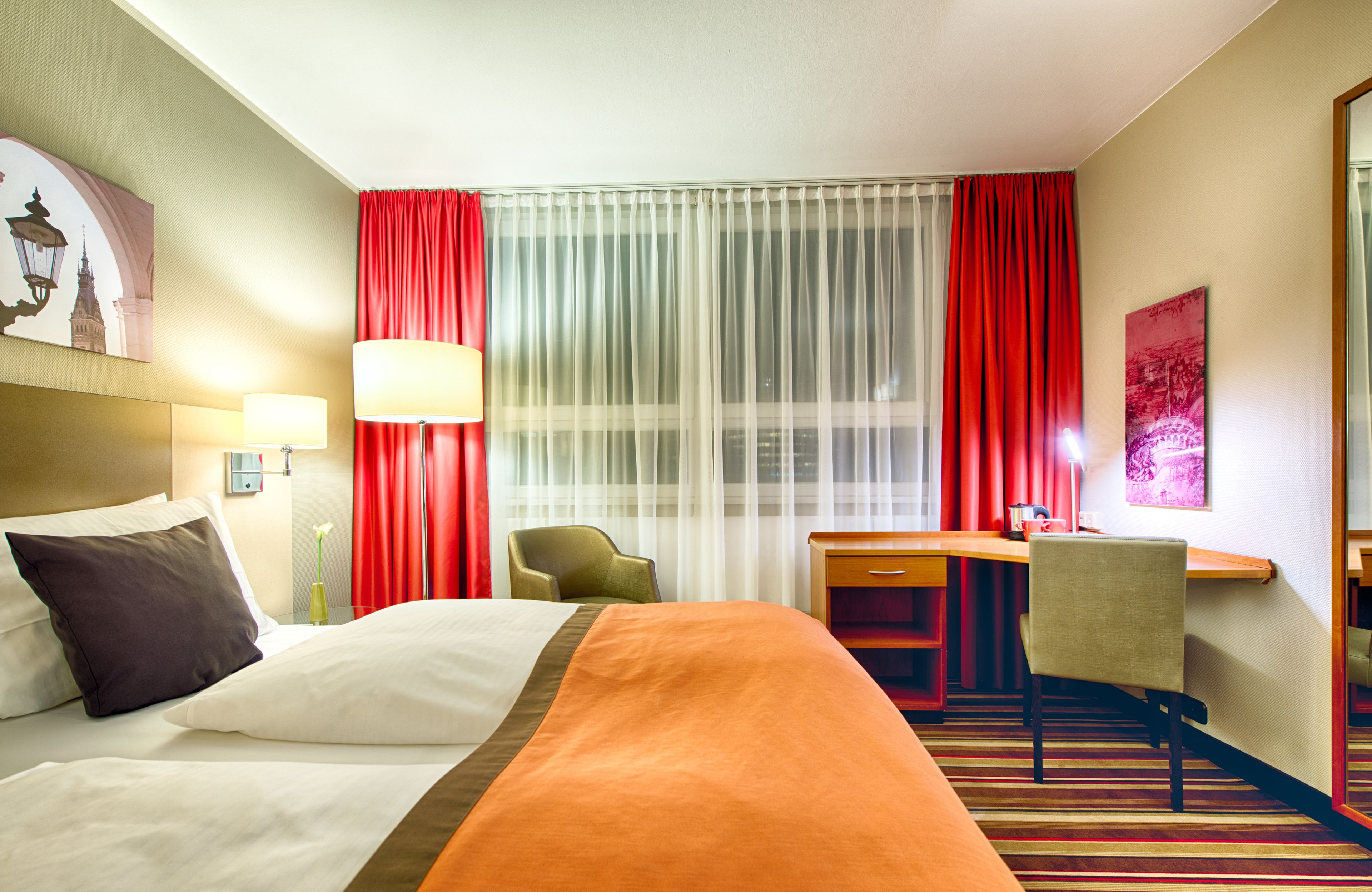 Habitación de hotel con cama, escritorio, silla y una ventana grande con cortinas.