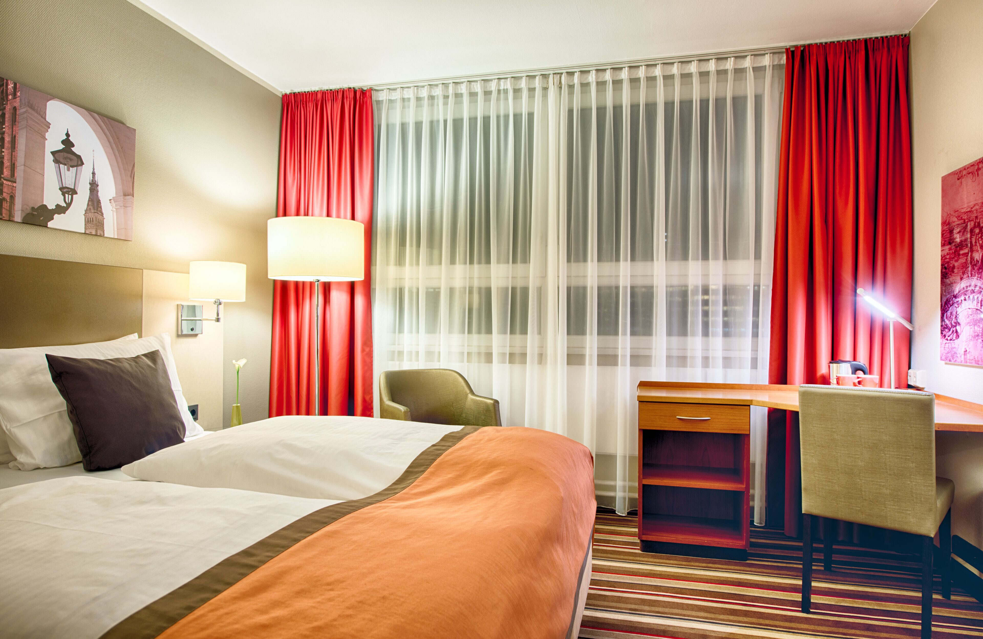 Una habitación de hotel con cama, escritorio, silla y cortinas.
