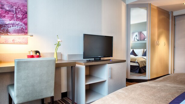 Ett modernt hotellrum med en platt-TV, ett skrivbord med en stol, en säng och en garderob.