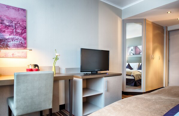 Una habitación de hotel moderna con televisión de pantalla plana, un escritorio con silla, una cama y un armario.