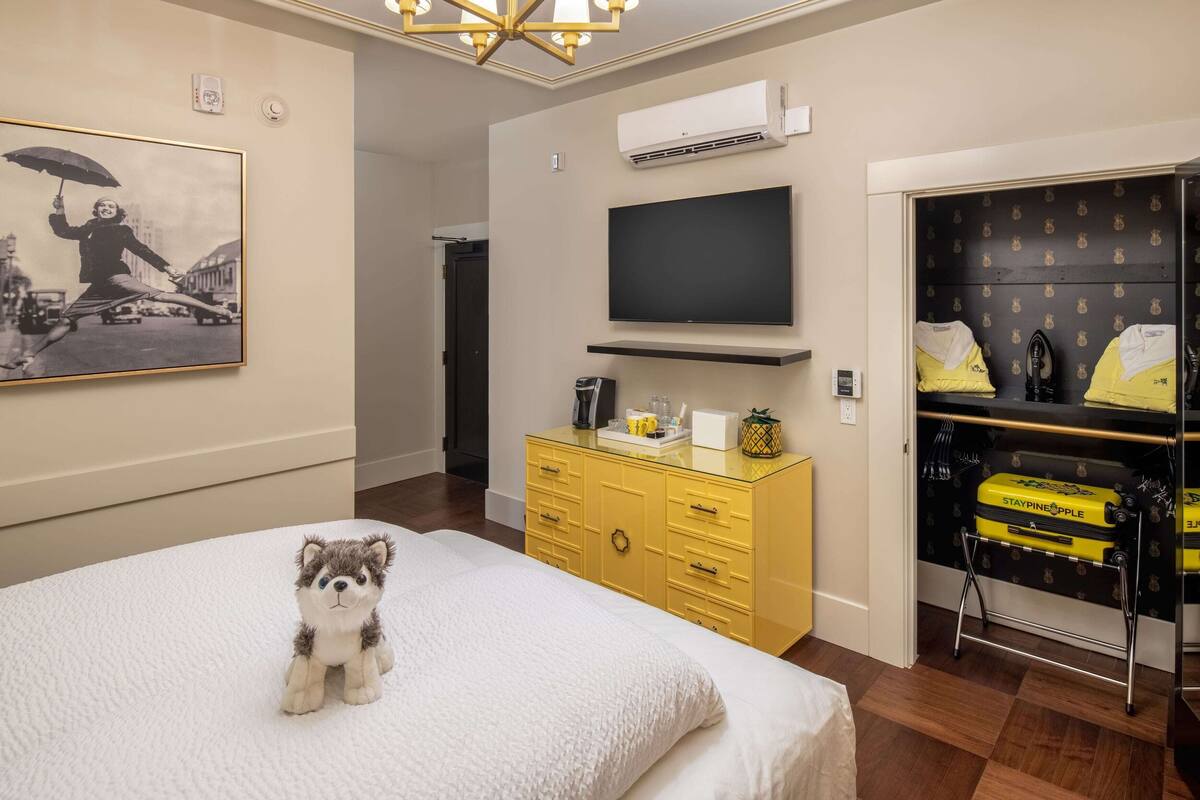 A hotel room with a bed, a television, a wardrobe, and a small stuffed animal on the bed.