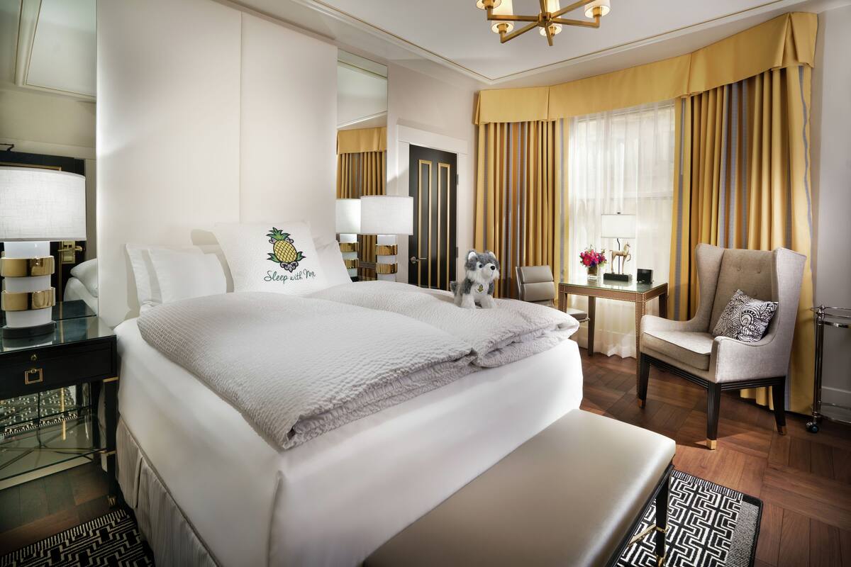 A hotel room with a large bed, a desk with a chair, a lamp, and a window with curtains.