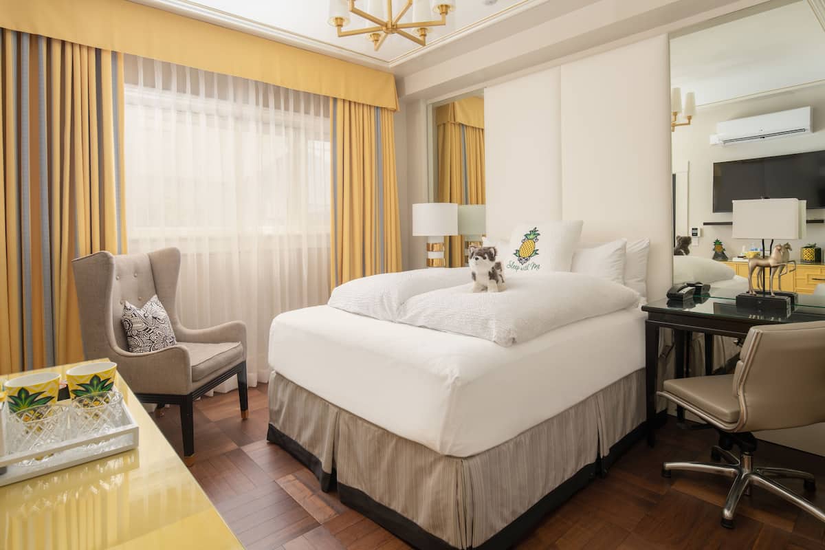A hotel room with a large bed, a desk with a chair, a TV, and a minibar.