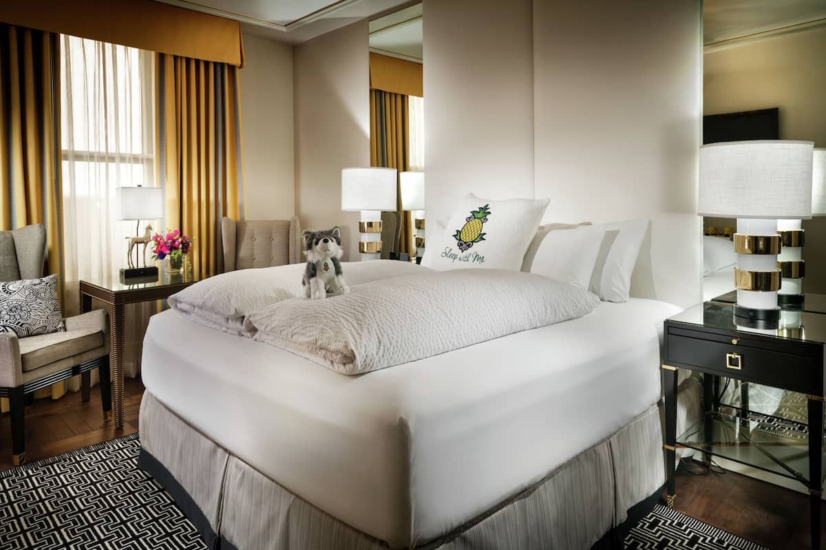 A hotel room with a large bed, a nightstand with a lamp, a chair, and a decorative pillow with a pineapple design.
