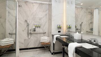 A modern bathroom with a glass-enclosed shower, marble walls, a black countertop sink, and a mirror.