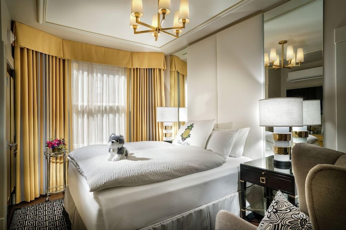 A hotel room with a large bed, a bedside table with a lamp, a chair, and a mirror.