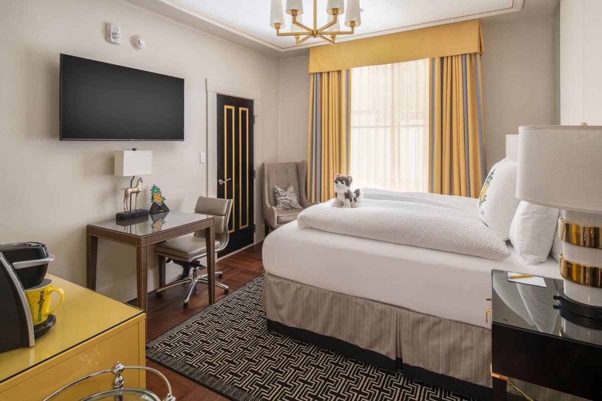 A hotel room with a bed, a desk, a chair, a TV, and a window with curtains.