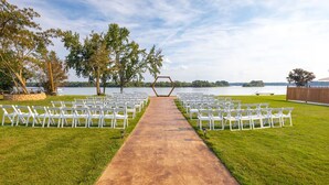 Decoración para ceremonia de boda con pasillo de concreto, sillas blancas a cada lado y un arco hexagonal al final.
