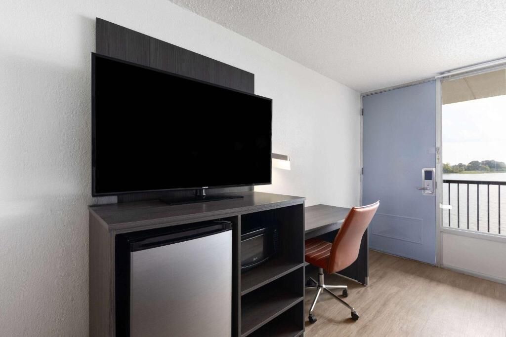 Una habitación moderna con televisor de pantalla plana en la pared, un escritorio con silla y una puerta corredera que da a un balcón.