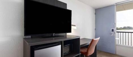 Una habitación moderna con televisor de pantalla plana en la pared, un escritorio con silla y una puerta corredera que da a un balcón.
