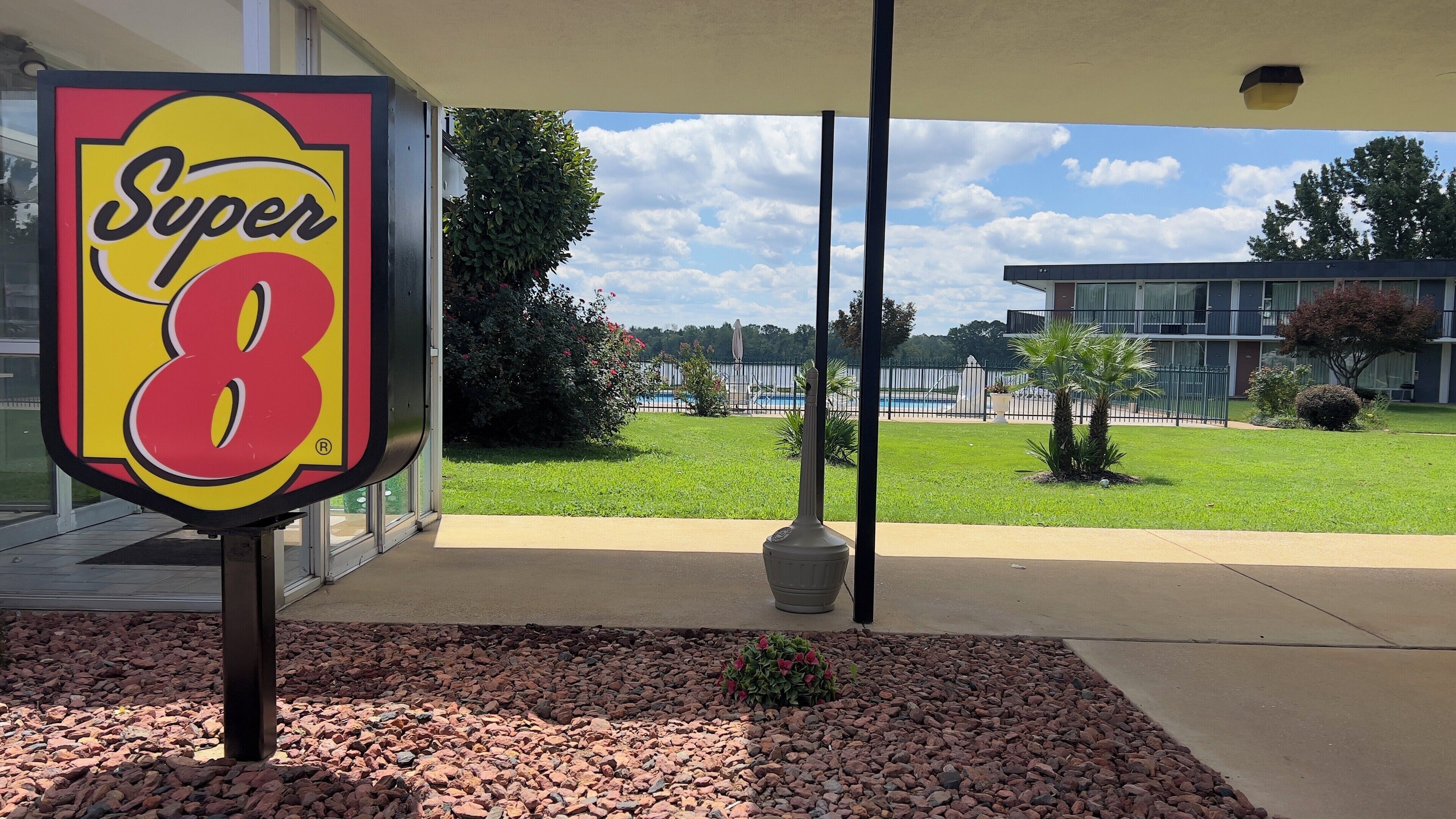 A Super 8 sign in front of a building with a pool and a well-maintained lawn.