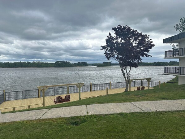 A waterfront property with a wooden deck, a bench, and a tree.