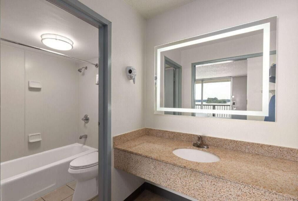 A modern bathroom with a white bathtub, a sink with a granite countertop, and a large mirror.