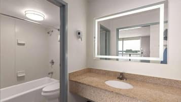 A modern bathroom with a white bathtub, a sink with a granite countertop, and a large mirror.