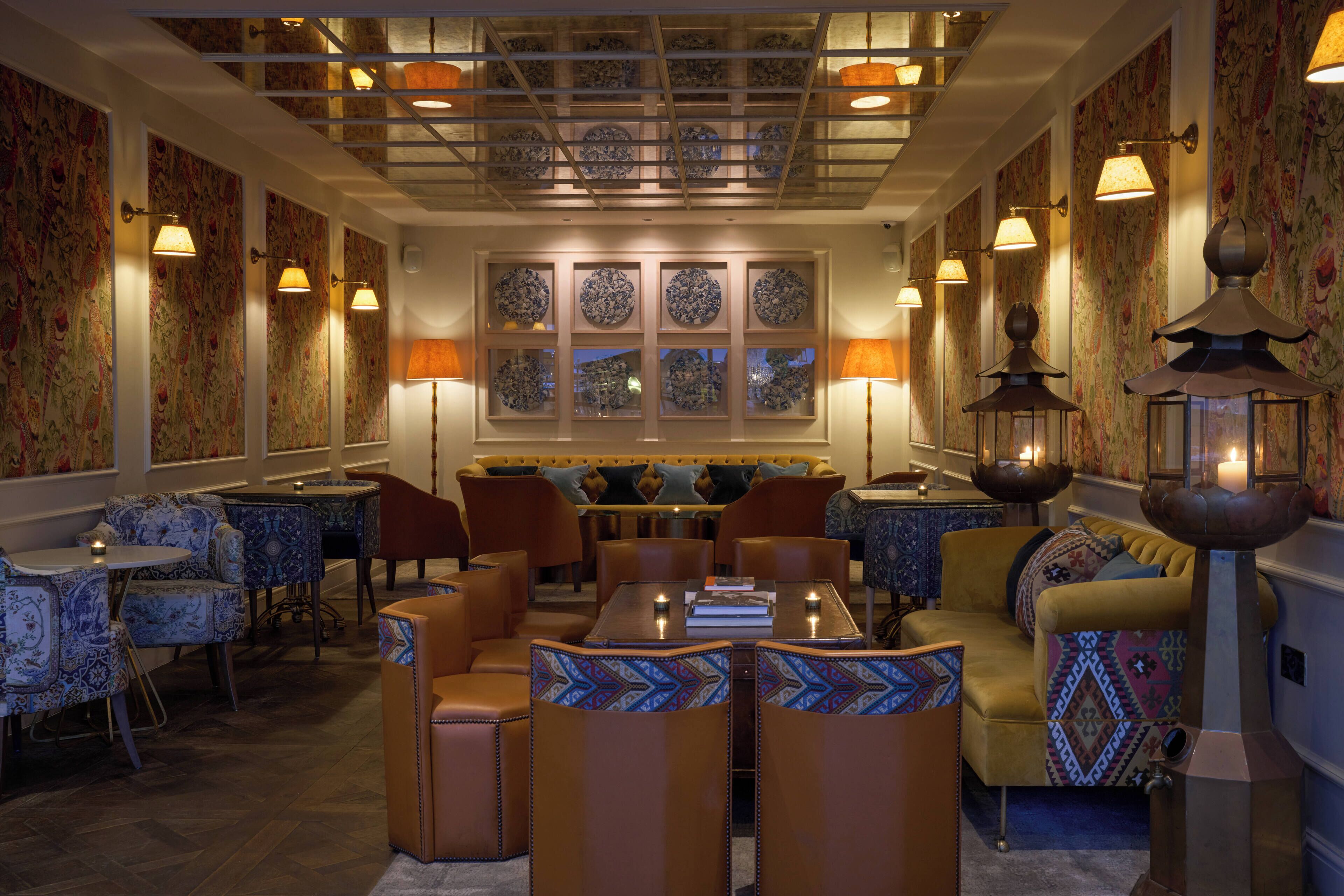 A well-lit lounge area with patterned wallpaper, a central seating arrangement, and decorative wall sconces.