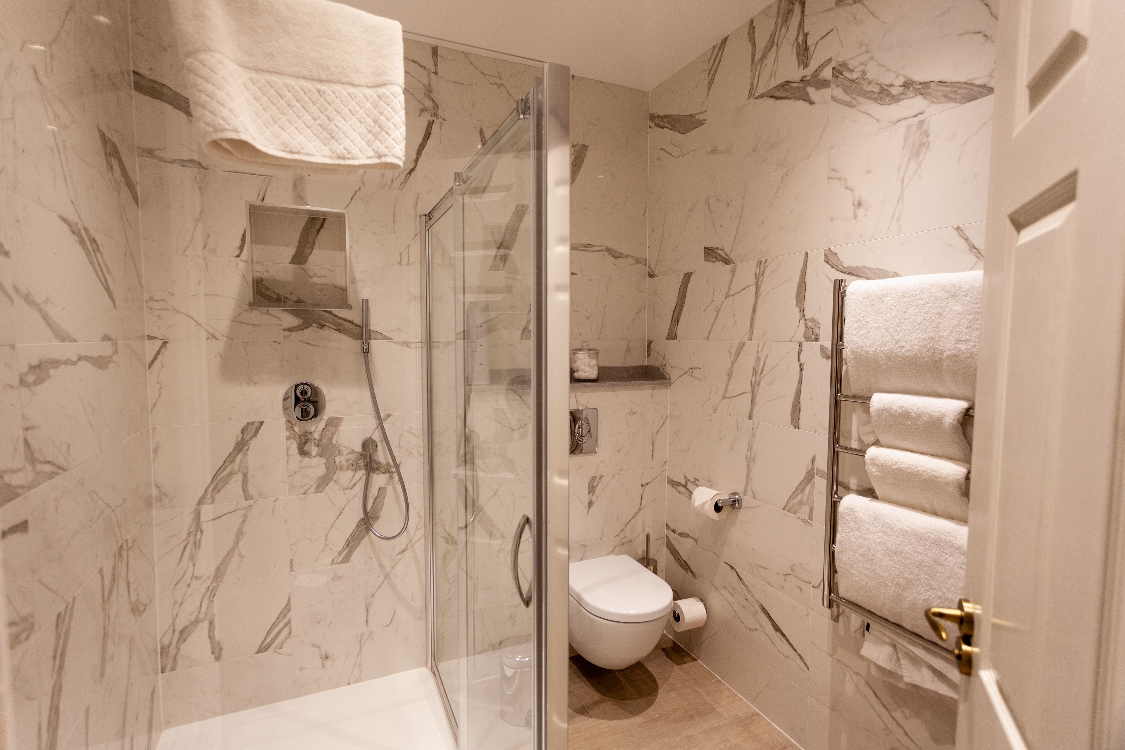 Une salle de bain avec une douche à parois de verre, des toilettes et des murs décorés d’un motif marbré.