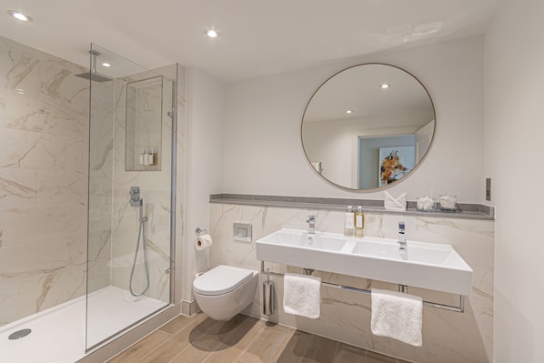 Un baño moderno con ducha de vidrio, inodoro blanco y lavamanos doble con un espejo grande arriba.