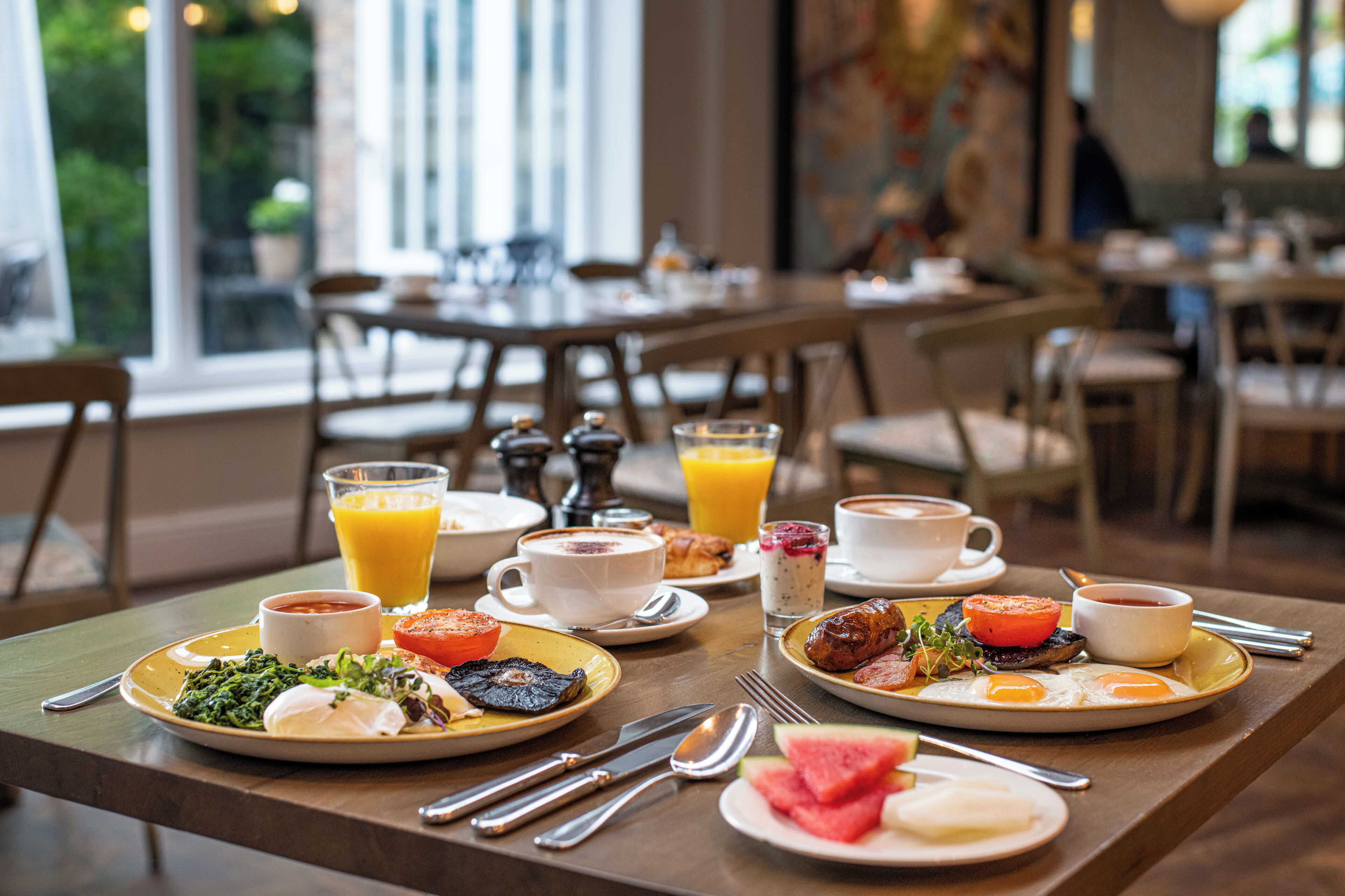 A breakfast setting with plates of food, beverages, and cutlery on a wooden table.