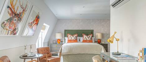 A modern hotel room with a large bed, a desk, a chair, and artwork on the walls.