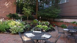 A patio area with a round metal table and chairs, surrounded by a garden with various plants and flowers. - The Salem Inn (Salem)