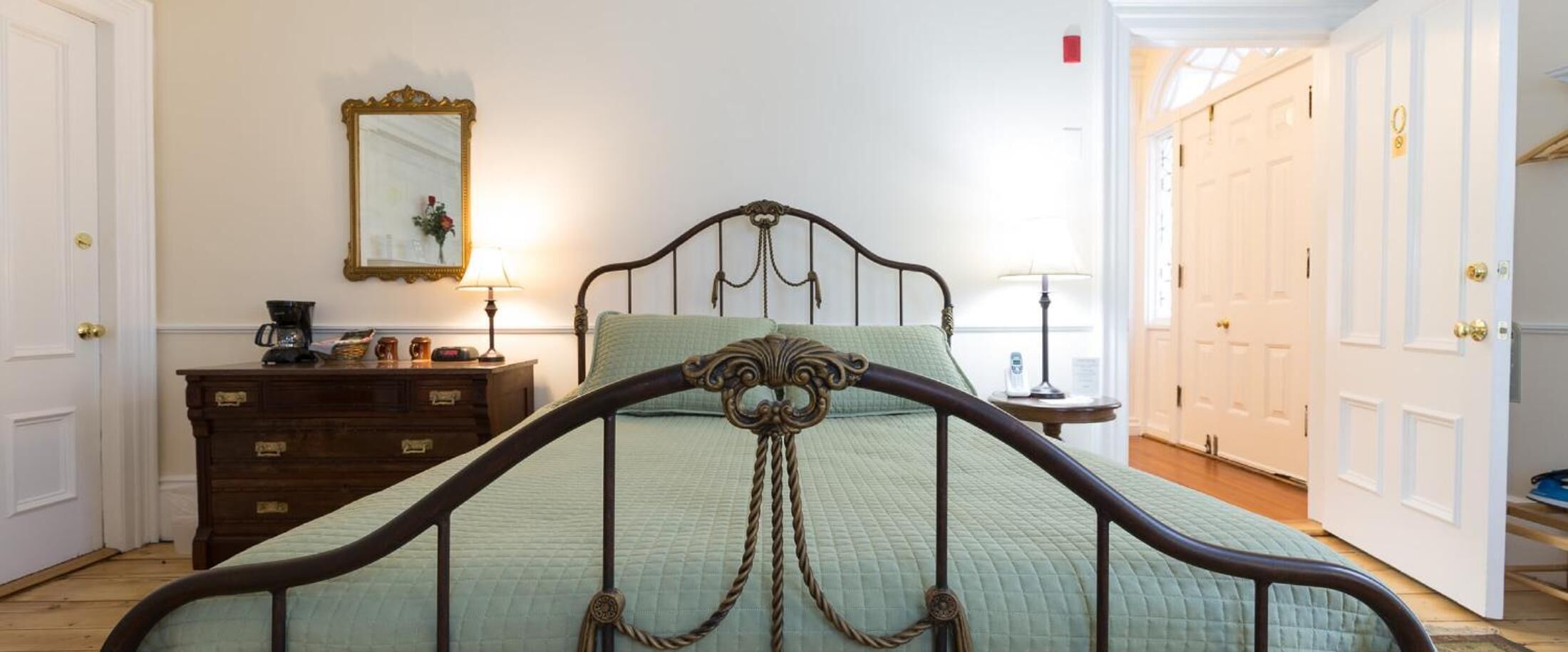 A bedroom with a bed, dresser, mirror, and two doors.