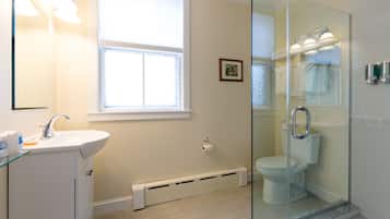 Ein modernes Badezimmer mit Duschkabine aus Glas, einem weißen Waschbecken und einem Fenster für Tageslicht.