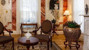 A room with two armchairs, a small round table, and a decorative vase. There is a large window with sheer curtains and a fireplace with a vase on the mantel. - The Salem Inn (Salem)