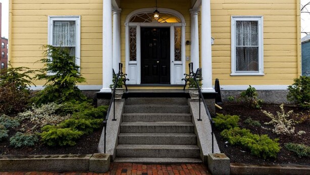 A yellow building with a black door, white columns, and a brick pathway leading to the entrance. - The Salem Inn (Salem)