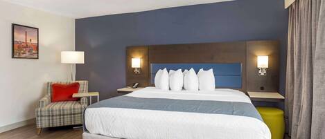 Une chambre d’hôtel avec un grand lit, une chaise, une table de chevet et une lampe.