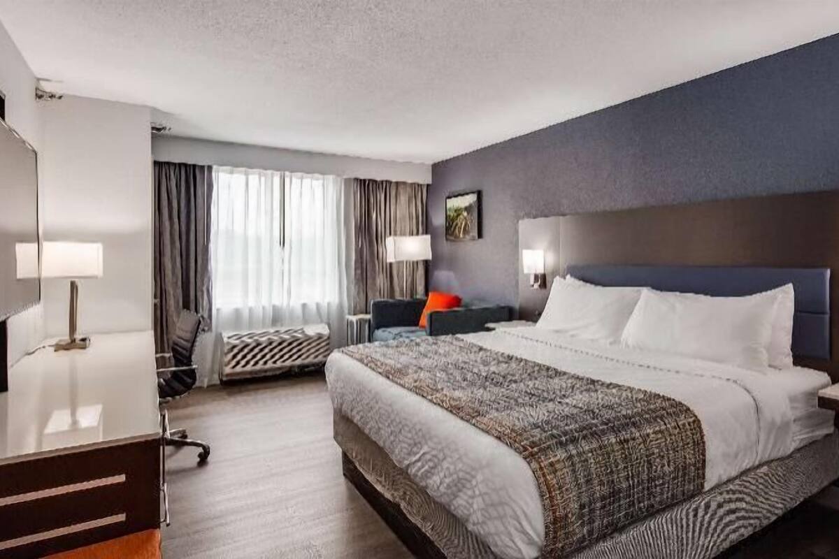 Een hotelkamer met een groot bed, een bureau, een stoel, een bureaulamp, een nachtkastje, een lamp en een raam met gordijnen.
