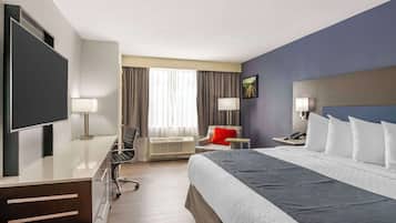 Habitación de hotel con cama, escritorio, silla, televisor, lámpara y ventana con cortinas.