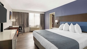 Une chambre d’hôtel avec un grand lit, un bureau, une chaise, une télévision et une fenêtre avec des rideaux.