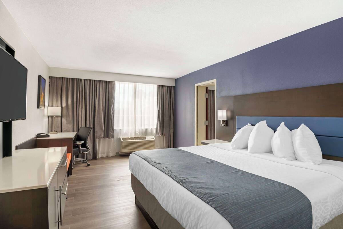 Een hotelkamer met een groot bed, een bureau, een stoel, een televisie en een raam met gordijnen.