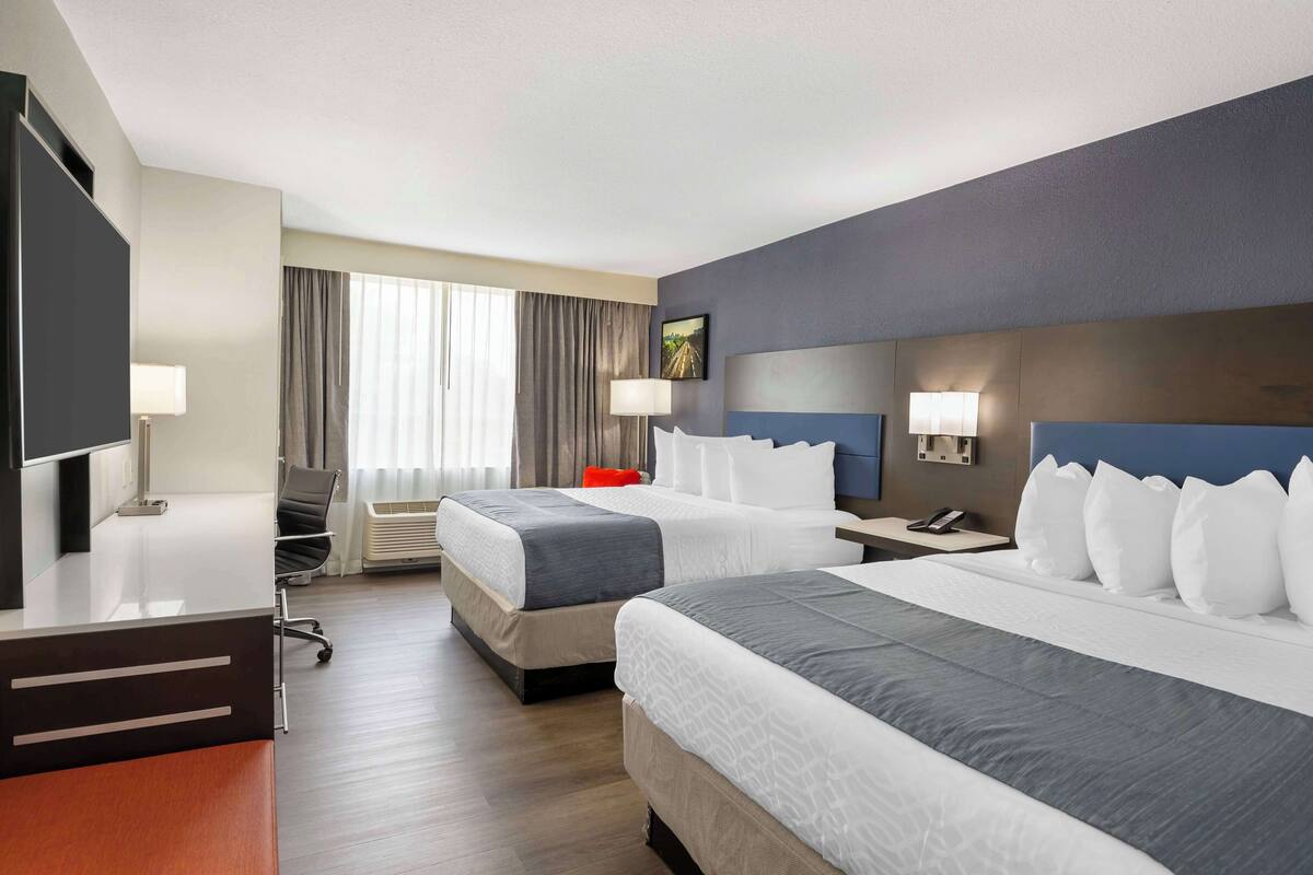 Een hotelkamer met twee bedden, een bureau, een stoel, een televisie en een raam met gordijnen.