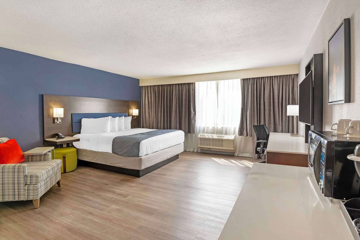 Een hotelkamer met een bed, een bureau, een stoel, een televisie en een raam met gordijnen.
