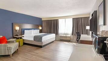 A hotel room with a bed, a desk, a chair, a TV, and a window with curtains.