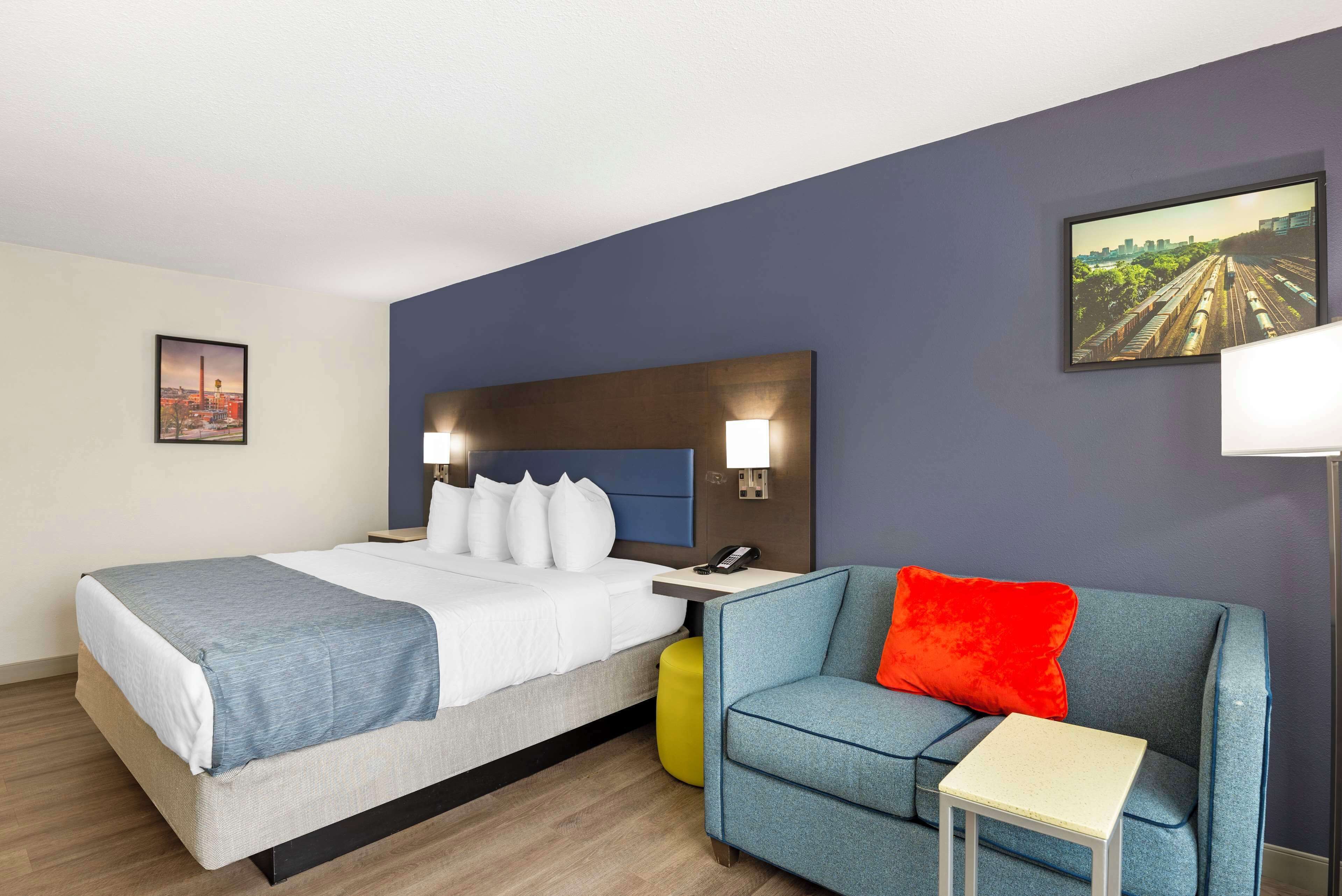 A hotel room with a bed, a blue sofa, a small table, and a nightstand with a lamp.