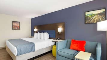 A hotel room with a bed, a blue sofa, a small table, and a nightstand with a lamp.