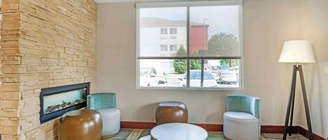 A lobby with a stone wall, a fireplace, two round tables, and chairs.