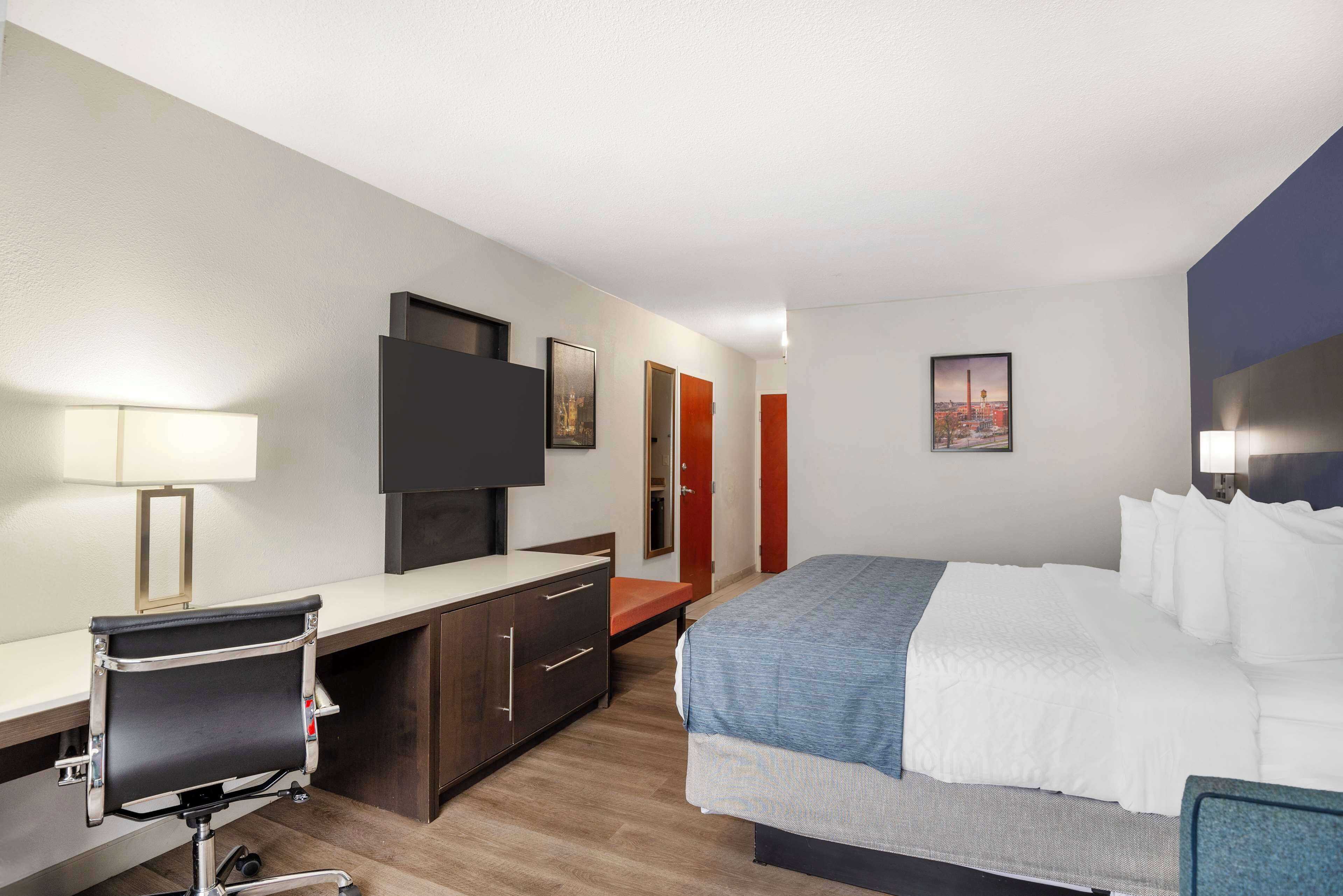 A hotel room with a bed, desk, chair, TV, and artwork on the walls.