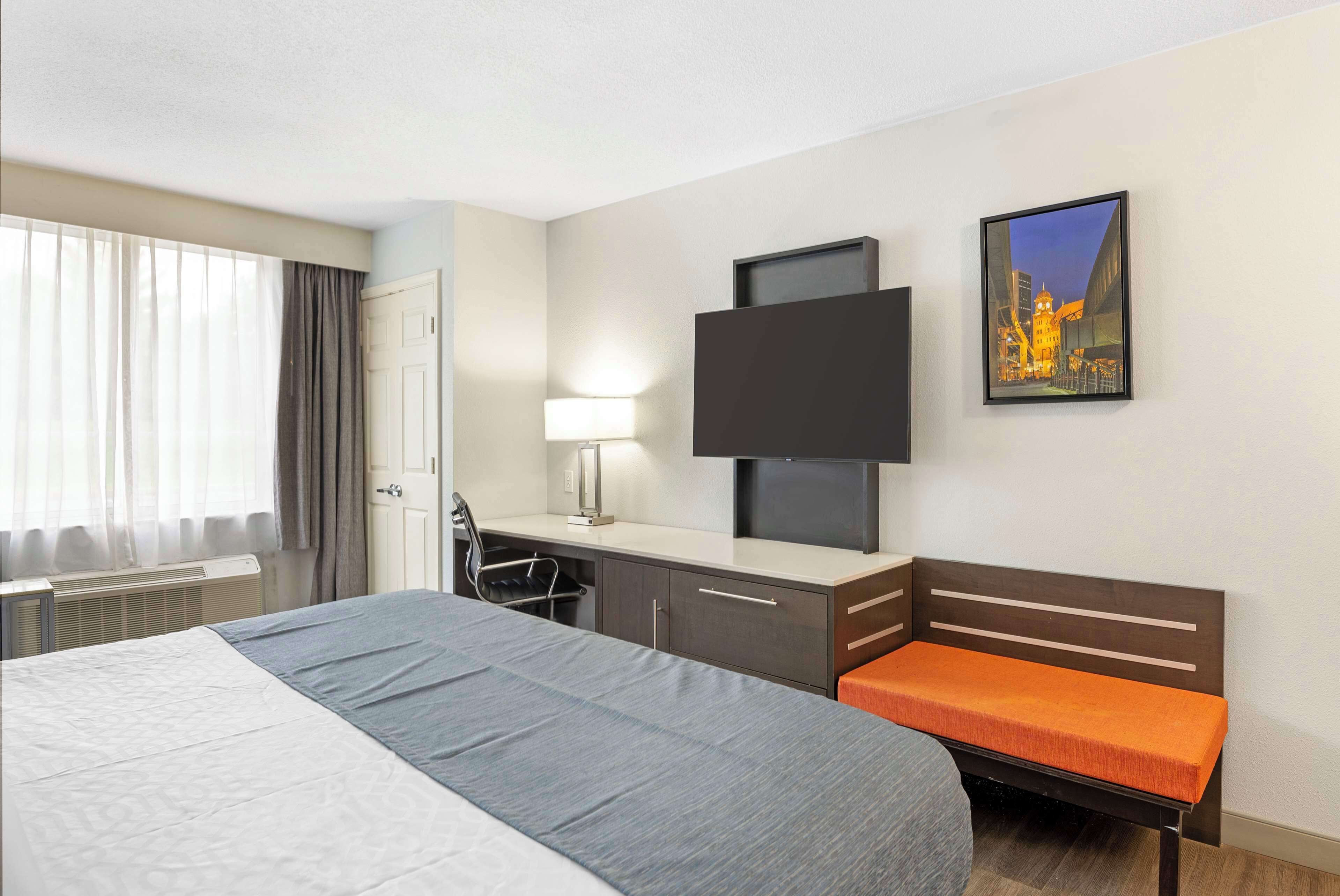 A hotel room with a bed, desk, chair, and a TV mounted on the wall.