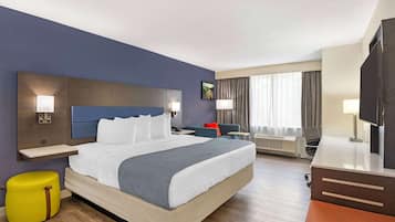 Habitación de hotel con una cama grande, un escritorio, una silla, un televisor y una ventana con cortinas.