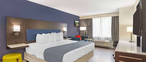 A hotel room with a large bed, a desk, a chair, a TV, and a window with curtains.