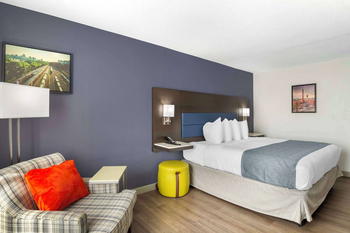 Een hotelkamer met een bed, een stoel, een klein tafeltje, een nachtkastje en een wandplank met een telefoon en lamp.