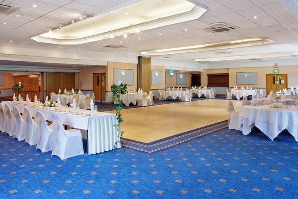 A large conference room with multiple tables set for a formal event, featuring white tablecloths and chairs with white sashes.
