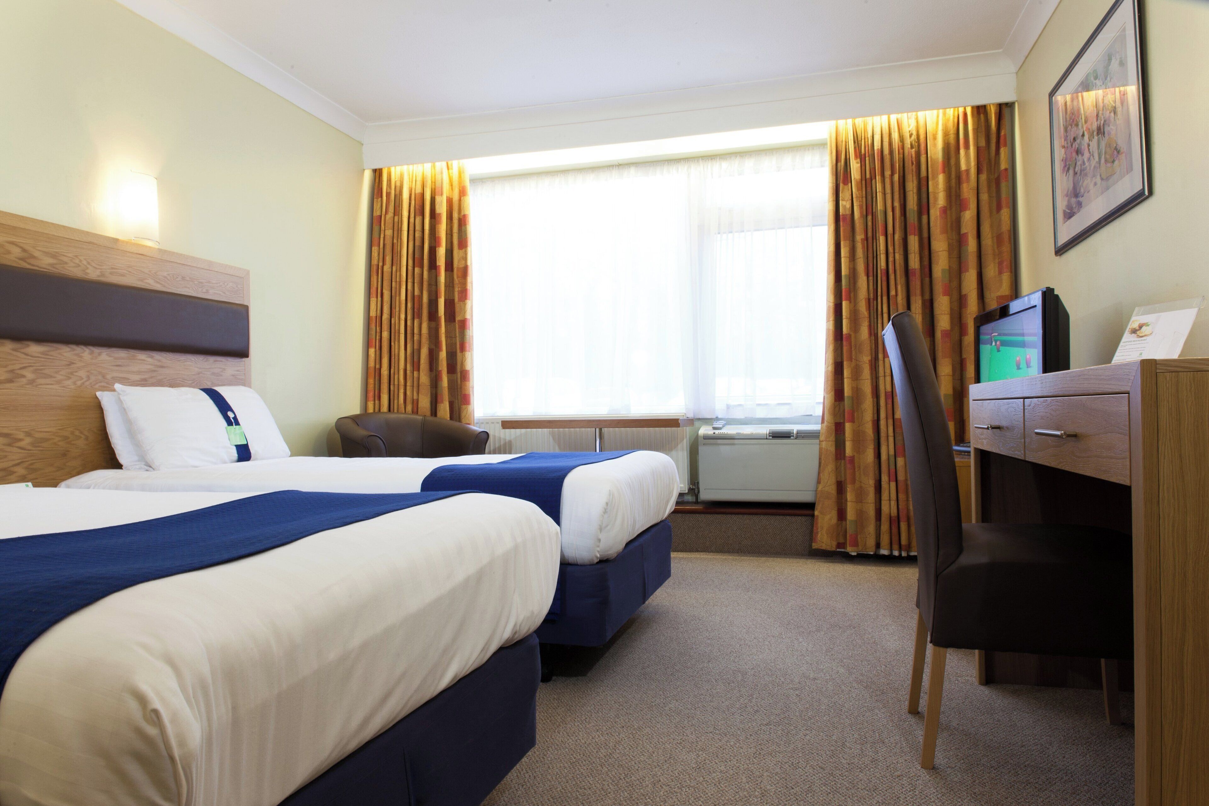 A hotel room with two beds, a desk, a chair, and a window with curtains.